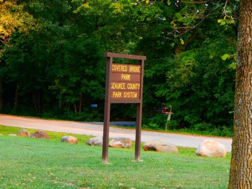Sign for Covered Bridge Park in the Ozaukee County Park System, surrounded by trees and grassy area.