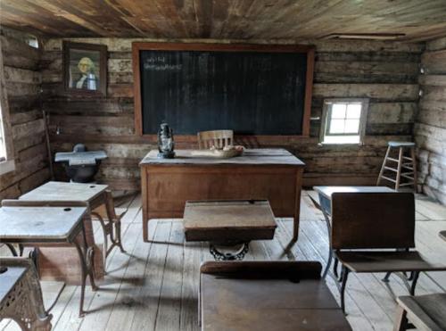 A rustic classroom with wooden desks, a chalkboard, and a teacher's desk, featuring a vintage atmosphere.