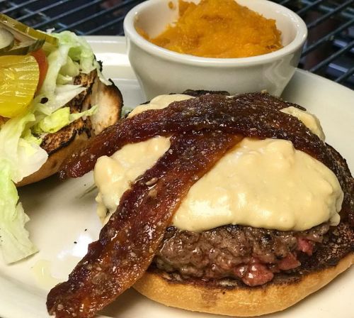 A juicy burger topped with melted cheese and crispy bacon, served with a side of sweet potato mash and a lettuce-topped bun.