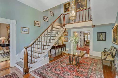 A spacious foyer with a staircase, elegant decor, and framed artwork on the walls, featuring a patterned rug.