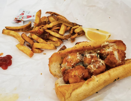 A fried seafood sandwich with sauce, served with a side of crispy French fries and a lemon wedge.