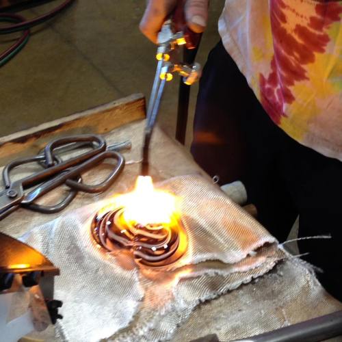 A person using a torch to shape molten glass, creating a colorful design on a work surface.