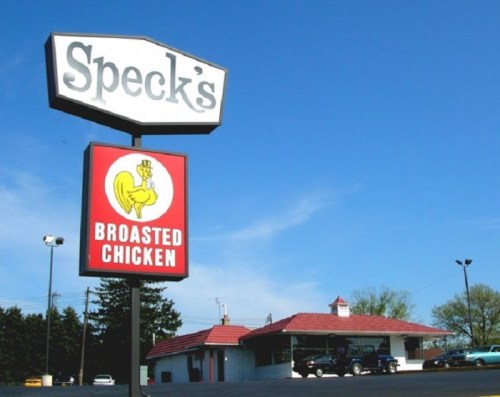Sign for Speck's Broasted Chicken with a restaurant building and clear blue sky in the background.