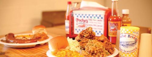 A table with plates of fried chicken, coleslaw, corn, rolls, and various sauces in colorful containers.