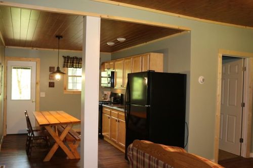 Cozy cabin interior featuring a dining table, kitchen with black appliances, and a living area with a sofa.