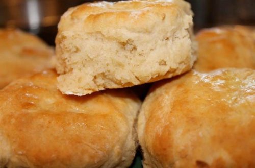 Golden-brown biscuits stacked together, with one biscuit partially cut to show its fluffy interior.