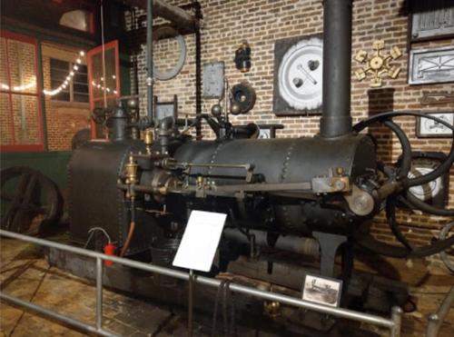 A vintage steam engine displayed in a museum, featuring intricate metalwork and historical artifacts in the background.