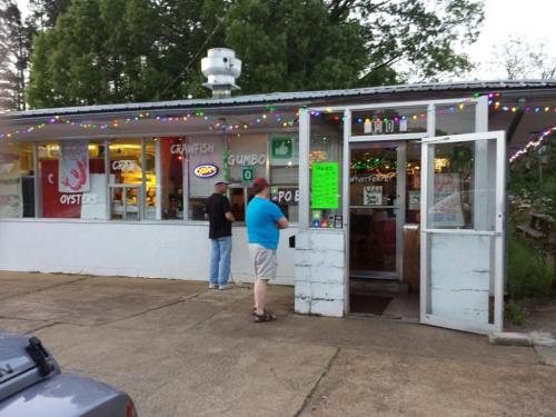 A small, colorful seafood restaurant with festive lights, featuring a sign for gumbo and customers waiting outside.
