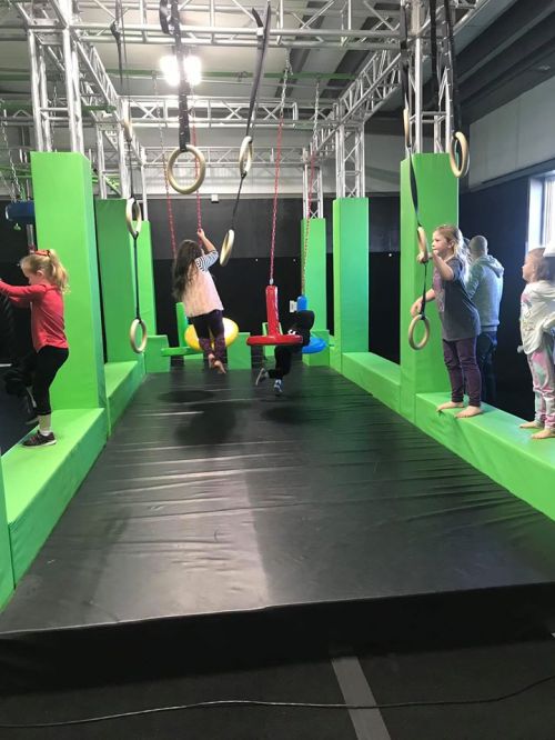 Children play on a colorful indoor obstacle course with rings and platforms, engaging in active fun.