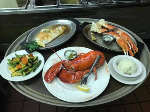 A tray with a lobster, crab legs, baked fish, mashed potatoes, and sautéed vegetables, garnished with lemon.