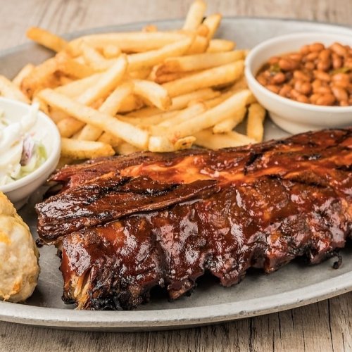 A plate featuring BBQ ribs, French fries, baked beans, and coleslaw on a rustic wooden table.
