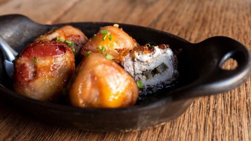 A cast iron dish with golden-brown dumplings, garnished with green onions, resting on a wooden table.