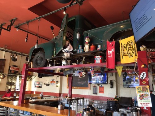 A vintage green truck is mounted on a bar's wall, surrounded by colorful decorations and memorabilia.
