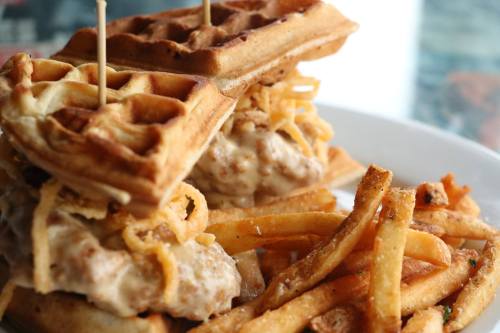 A plate featuring two waffles filled with fried chicken and topped with crispy onions, served with French fries.