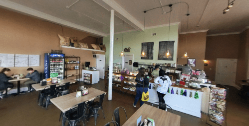 A cozy café interior with wooden tables, a counter displaying pastries, and customers ordering drinks.