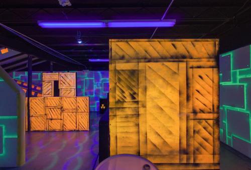 A brightly lit indoor space with neon accents, featuring painted crates and geometric patterns on the walls.