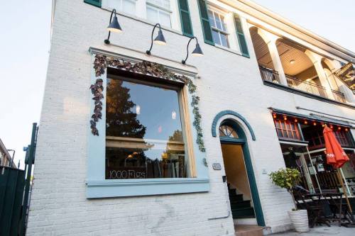 Exterior of a white brick building with green accents, featuring a window labeled "1000 Figs" and outdoor seating.