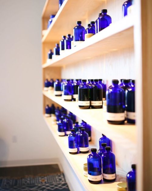 A wooden shelf displaying various blue glass bottles and jars, arranged neatly in a well-lit space.
