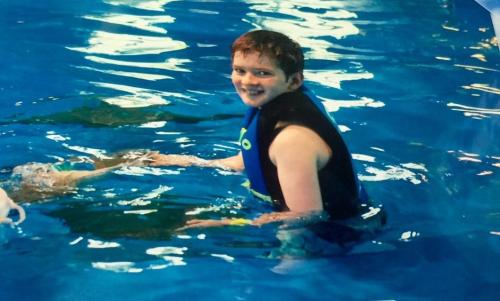 A smiling child in a life jacket enjoys swimming in a blue pool.