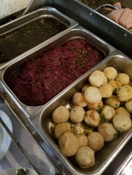Three metal trays with food: one with purple cabbage, one with a dark sauce, and one with golden-brown round dumplings.