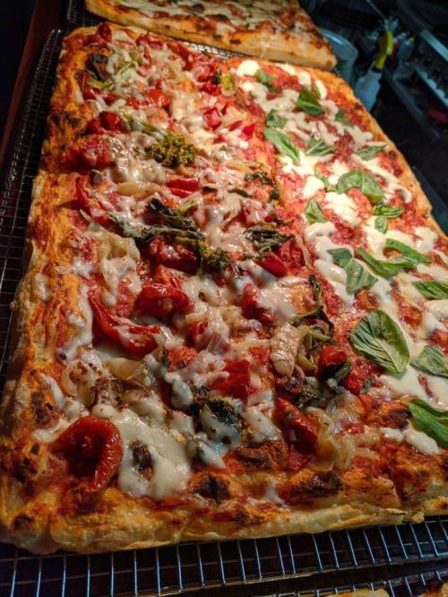 A close-up of a freshly baked pizza topped with tomatoes, broccoli, and fresh basil on a wire rack.