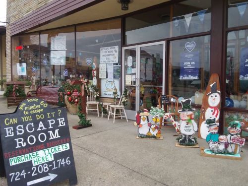 A storefront with an "Escape Room" sign, festive decorations, and wooden figures of snowmen and penguins outside.