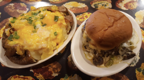 A loaded baked potato topped with cheese and green onions next to a cheeseburger with melted cheese on a plate.