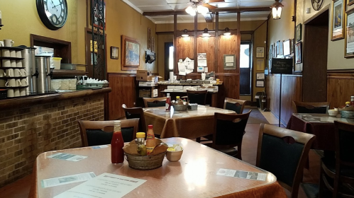Cozy restaurant interior with wooden decor, tables set with condiments, and a counter in the background.