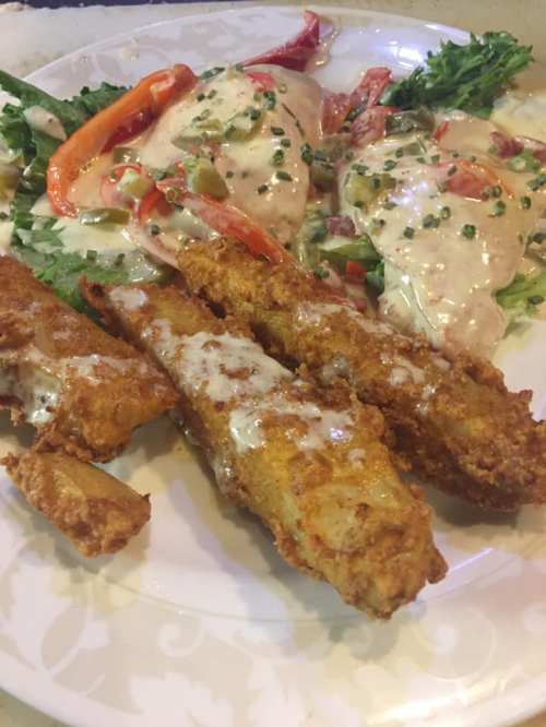 A plate of crispy fried fish sticks served with a fresh salad topped with creamy dressing and sliced vegetables.