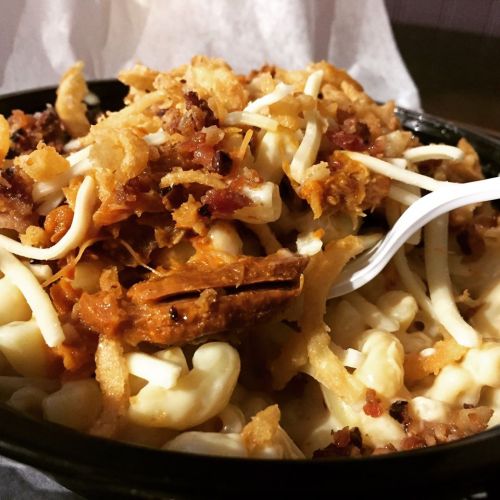 A close-up of a bowl of macaroni topped with crispy onions, cheese, and bacon bits, with a fork resting inside.