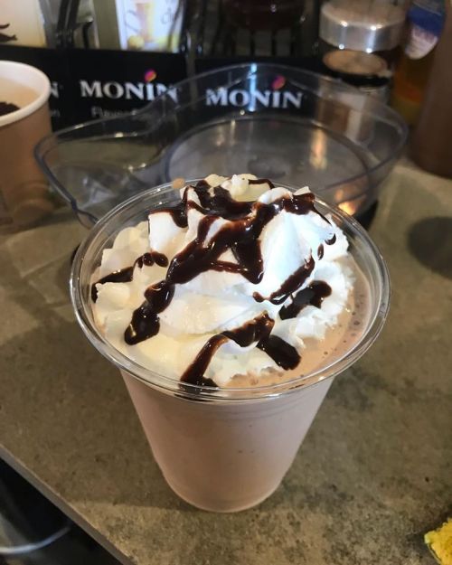 A creamy chocolate milkshake topped with whipped cream and drizzled with chocolate sauce in a clear cup.