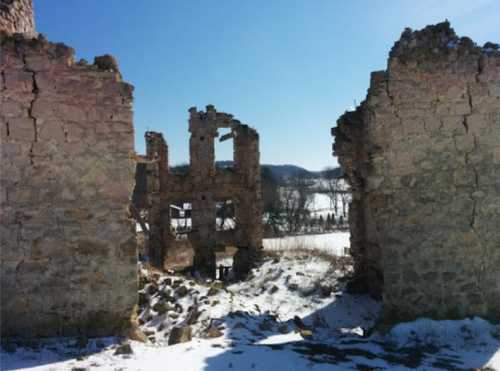 Ruins of a stone building with cracked walls, set against a clear blue sky and snowy landscape.