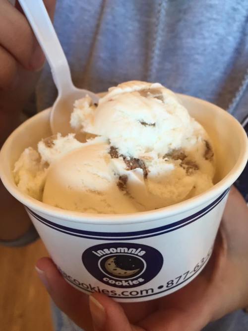 A person holding a cup of ice cream with cookie pieces, featuring a spoon for serving.