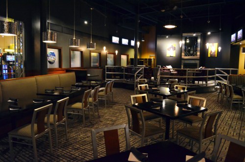 Modern restaurant interior with dark walls, tables set for dining, and a cozy atmosphere featuring wall art and lighting.