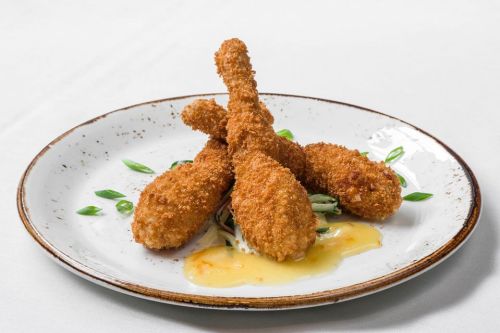 Three crispy fried chicken drumsticks on a white plate, garnished with green onions and served with a creamy sauce.