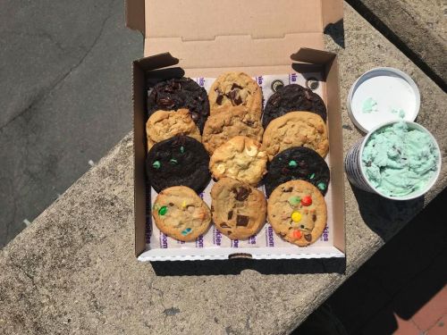 A box of assorted cookies and a container of mint chocolate chip ice cream on a concrete surface.