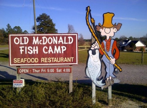 Sign for Old McDonald Fish Camp, featuring a cartoon fisherman holding a large fish, with restaurant hours listed.