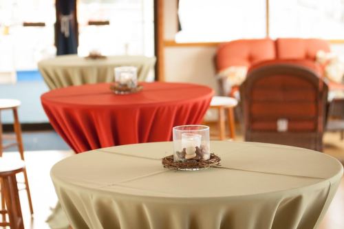 Two round tables with tablecloths in red and beige, each featuring a candle in a glass holder and decorative stones.