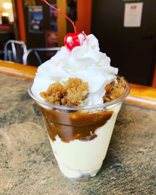 A dessert cup with layers of vanilla ice cream, chocolate sauce, crumbled cookie, topped with whipped cream and a cherry.