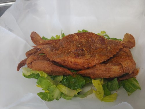 A fried soft-shell crab served on a bed of fresh lettuce, seasoned with spices.