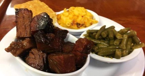 A plate featuring tender smoked meat, macaroni and cheese, green beans, and a crispy bread slice.