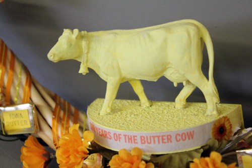 A yellow butter sculpture of a cow, labeled "14 Years of the Butter Cow," surrounded by decorative flowers.