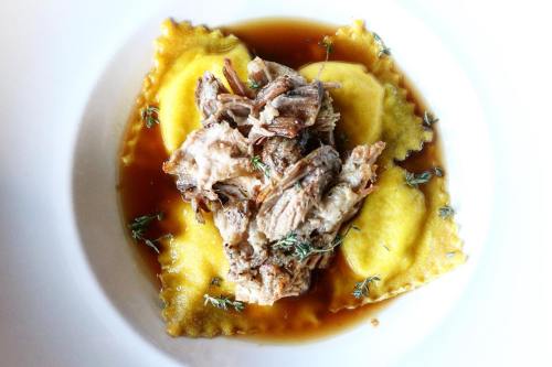 A plate of ravioli topped with shredded meat and garnished with thyme in a rich broth.