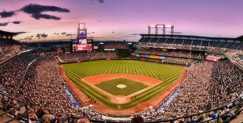 A panoramic view of a packed baseball stadium at sunset, with fans enjoying a game on the field.