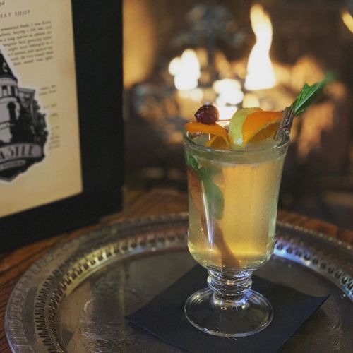 A refreshing cocktail garnished with fruit, served on a silver tray in front of a cozy fireplace.