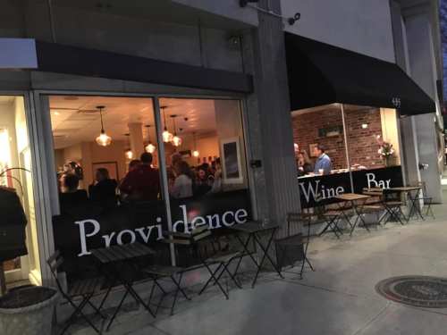 A cozy wine bar named "Providence" with outdoor seating, bustling with patrons inside during the evening.