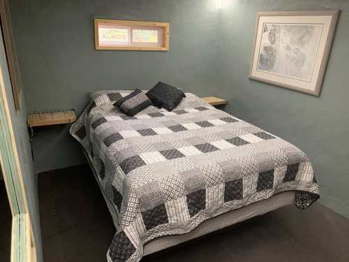 Cozy bedroom featuring a bed with a patterned quilt, two small side tables, and a framed artwork on the wall.
