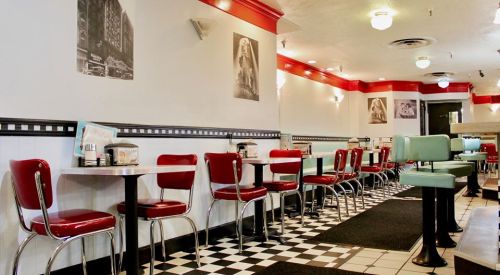Retro diner interior with red and teal seating, checkered floor, and black-and-white wall art.