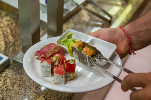 A hand holding a plate with sushi rolls, sashimi, and a small dish of green wasabi.