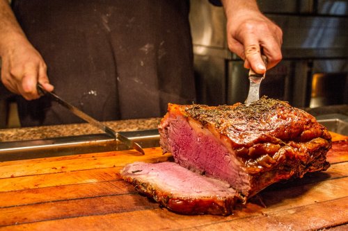 A chef slices a perfectly cooked roast on a wooden cutting board, showcasing its juicy pink interior.